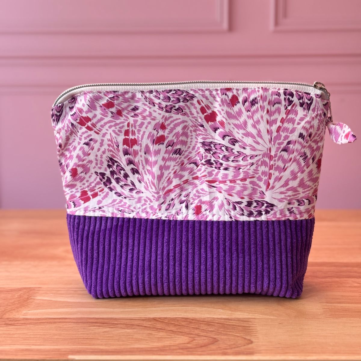 Trousse artisanale pour femme, motif de plumes stylisées dans les tons roses et violets, partie basse en velours côtelé violet profond.