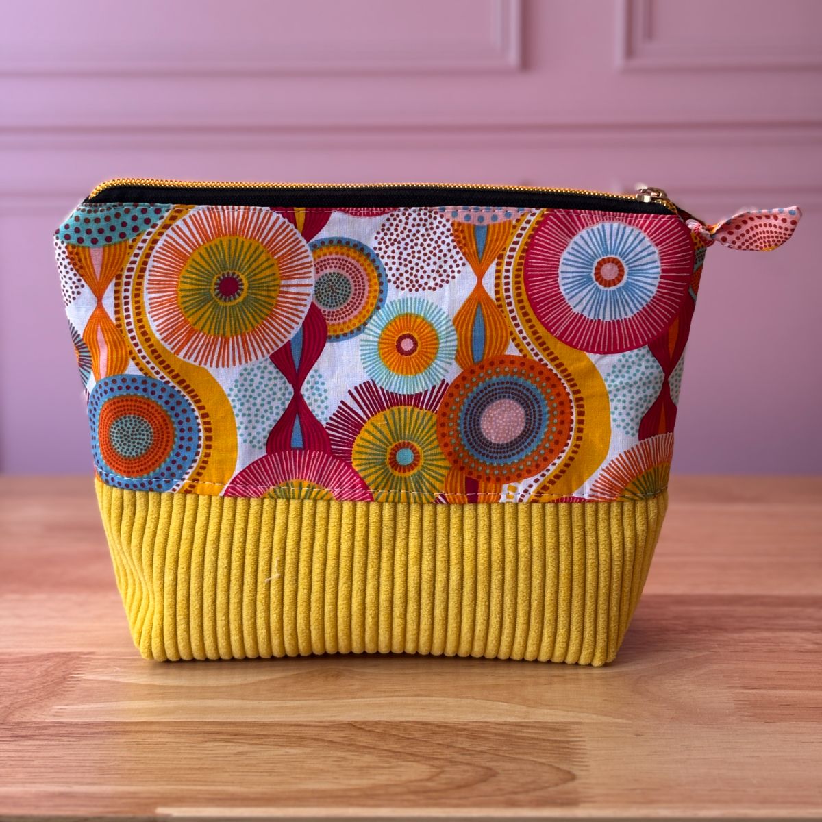Trousse de toilette en coton aux motifs graphiques de cercles multicolores (jaune, rouge, bleu) et bas en velours côtelé jaune moutarde.