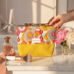 Trousse de maquillage colorée Maison Pivoine posée sur un marbre blanc avec des pivoines roses, un parfum et des pinceaux de maquillage.