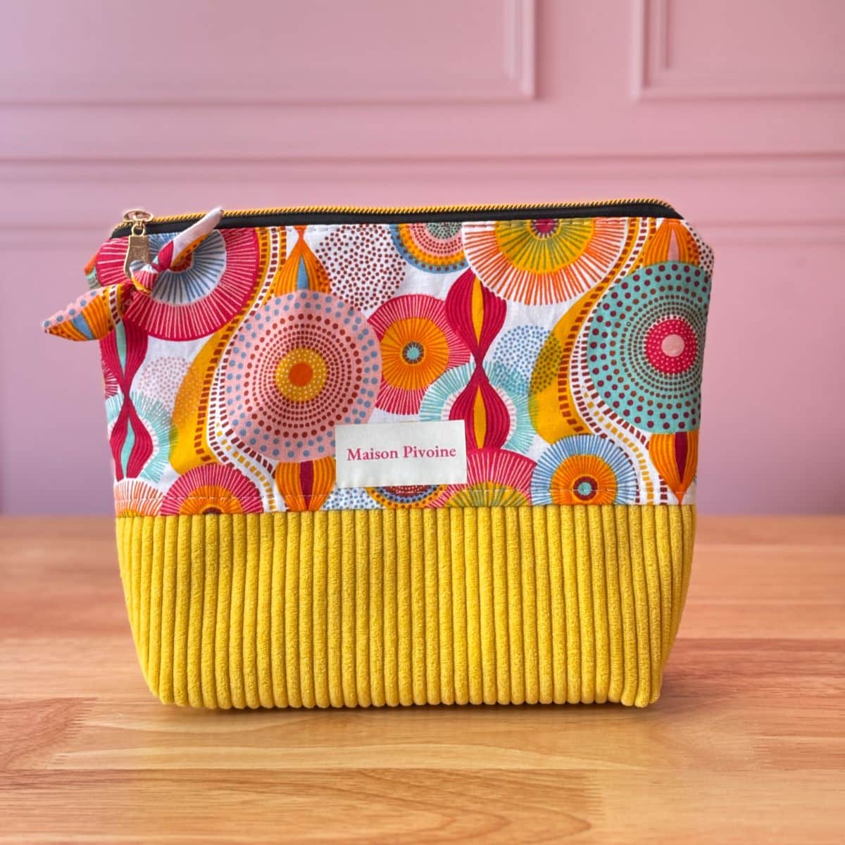 Pochette textile artisanale avec étiquette Maison Pivoine, imprimé ethnique chic et cercles colorés, fond en velours jaune vibrant.