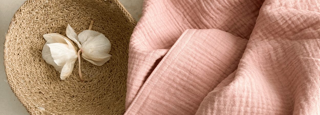 tissu gaze de coton dans les teinte rose posé à coté d'un panier avec une fleur d'orchidée dedans