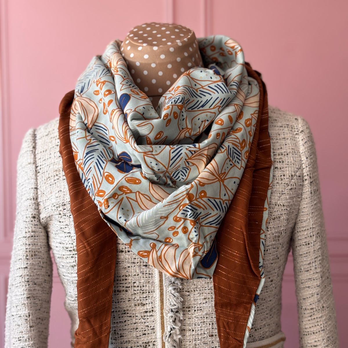 Le chèche signature Maison Pivoine en situation. Photographie professionnelle montrant le drapé réversible : d'un côté l'imprimé exclusif "Jardin Botanique" sur fond céladon, de l'autre la gaze de coton terracotta scintillant avec fils Lurex. Présenté sur une veste en tweed Maison Pivoine pour un look chic et intemporel.