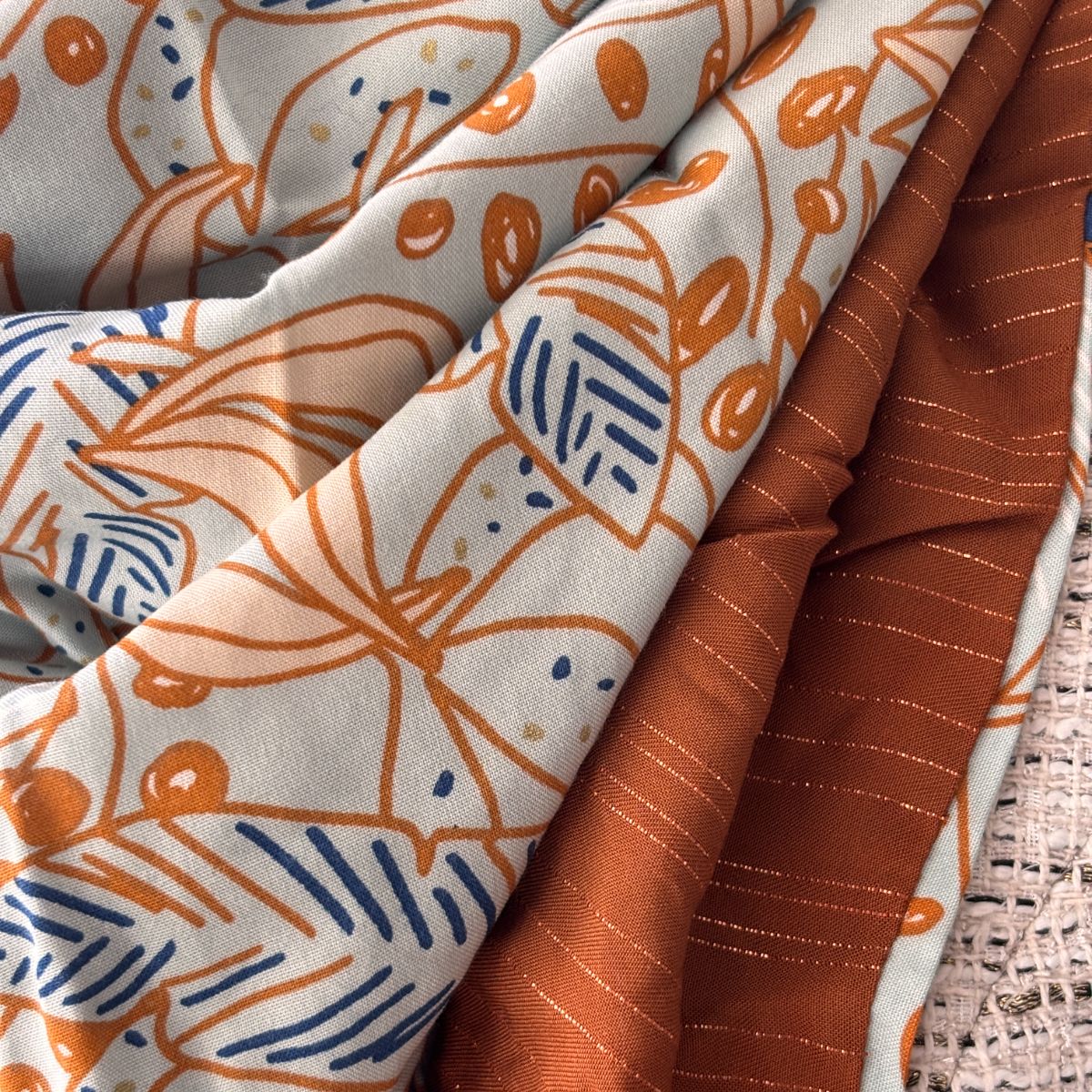 Zoom sur l'excellence textile Maison Pivoine. Détail du tissage haute qualité : contraste entre la fluidité de la viscose imprimée aux motifs botaniques exclusifs et la richesse texturée de la gaze de coton terracotta rehaussée de fils Lurex scintillants. La finesse des détails et la vibrance des couleurs sont mises en avant.