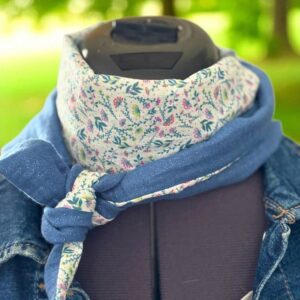 Écharpe fine et florale portée autour du cou, motif liberty et tissu bleu scintillant.