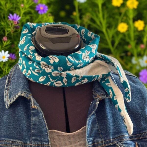 Mannequin couture portant une écharpe légère bleue canard à motif floral blanc, nouée autour du cou, sur fond de fleurs colorées et veste en jean.