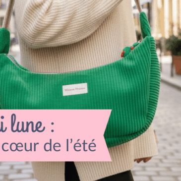 Femme portant un sac banane demi lune Cosmos en velours côtelé vert sur l'épaule, marchant dans une rue animée avec terrasses de café — accessoire tendance été, création artisanale Maison Pivoine.