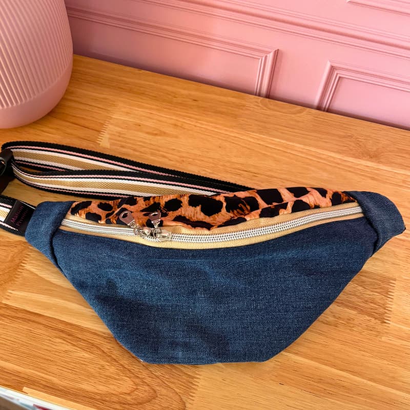 Sac banane Maison Pivoine en jeanโs recyclรฉ avec dรฉtail de sangle rรฉglable, posรฉ sur une table en bois.