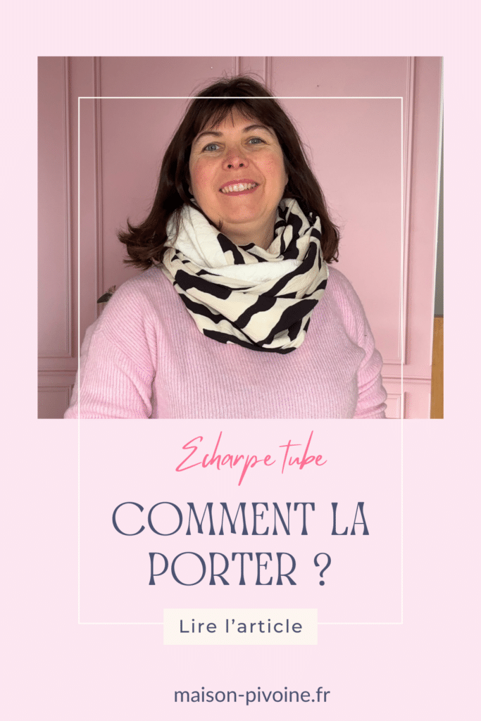 comment-porte-echarpe-tube Femme souriante portant une écharpe tube à imprimé zèbre noir et blanc et un pull rose pâle, posant devant un mur rose.