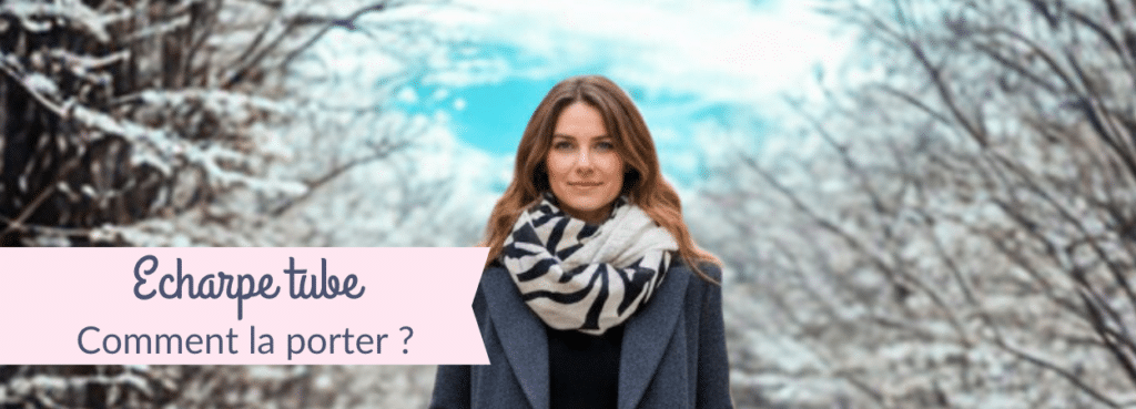 Femme marchant en hiver au milieu d’arbres enneigés, portant une écharpe tube zèbre et un manteau gris, avec le texte « Écharpe tube – Comment la porter ? »