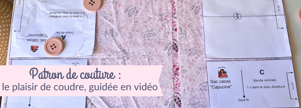 Vue de dessus d'un plan de travail de couture présentant les pièces d'un patron papier pour le « Sac cabas Capucine ». Les pièces blanches, maintenues sur un tissu rose à motifs par de gros boutons roses faisant office de poids, indiquent les instructions de coupe : « Corps de sac A » et « Bande centrale C ». Une bannière rose en bas à gauche affiche le texte : « Patron de couture : le plaisir de coudre, guidée en vidéo